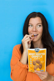 Woman eating honey roasted chipotle peanuts against a blue background