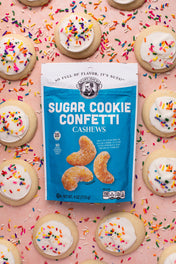 Packaging of Sugar Cookie Confetti Cashews with cookies and sprinkles in the background