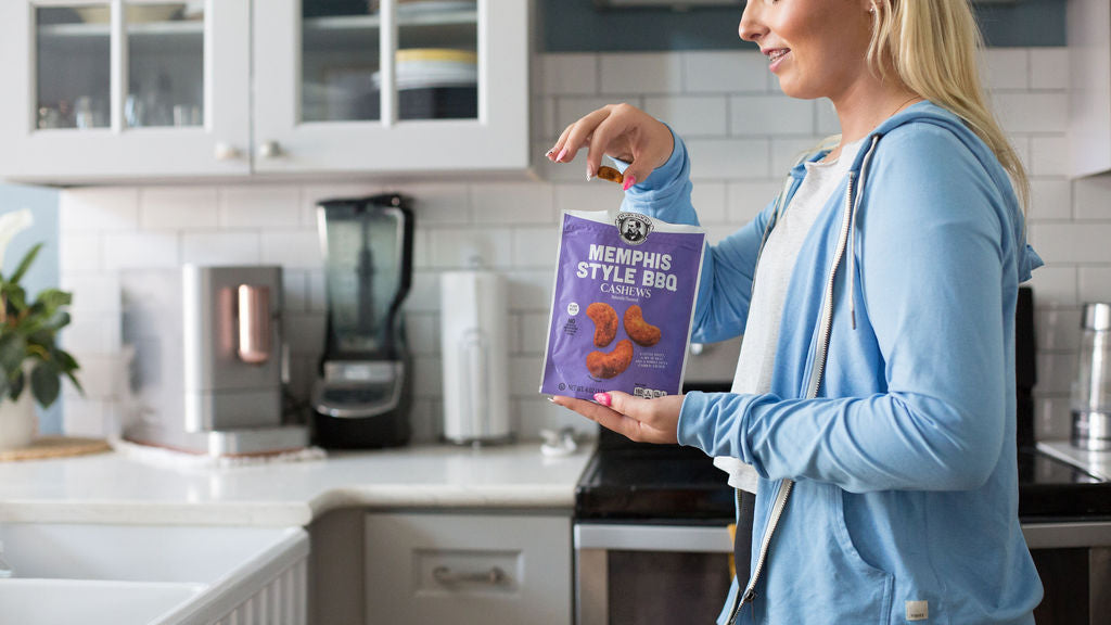 Woman holding a package of Memphis Style BBQ cashews in a kitchen.