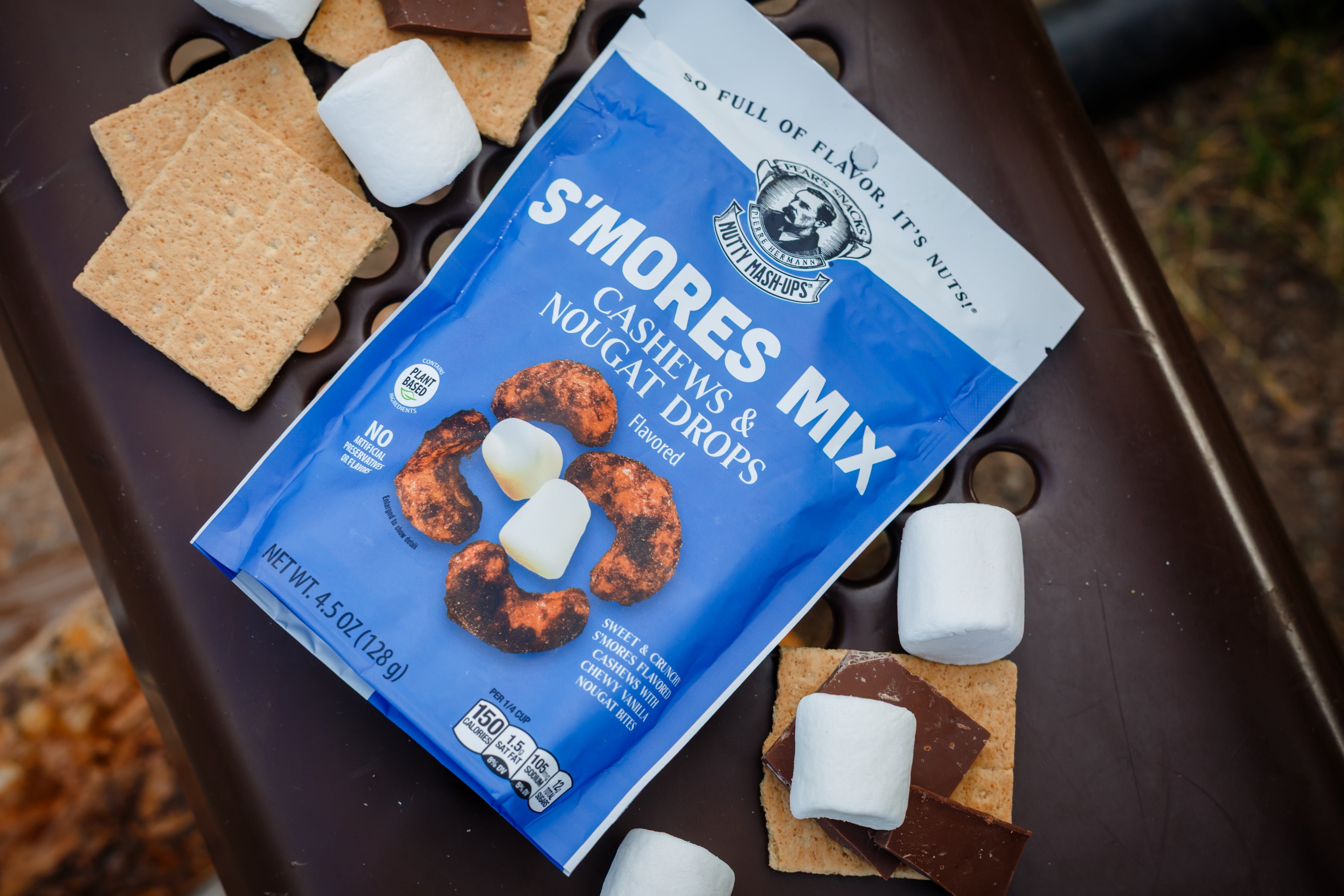 S'mores mix package with graham crackers, marshmallows, and chocolate on a picnic table bench at a camping site