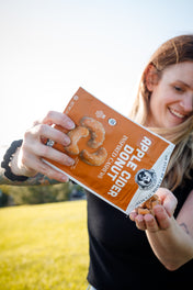 Person holding a bag of Apple Cider Donuts Cashews with a scenic background