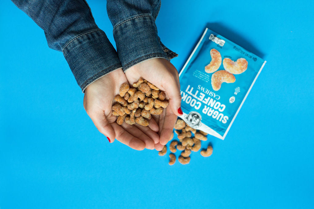 Person holding sugar cookie confetti cashews over a blue background